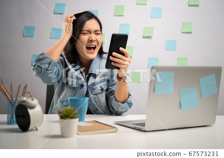 Asian woman angry looking at smart phone reading Asian woman angry looking at smart phone reading 67573231