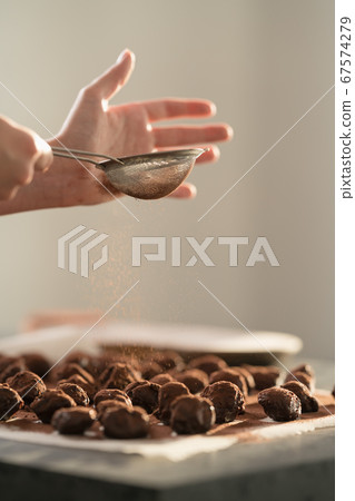 young woman sprinke truffles candy with cocoa powder on kitchen 67574279