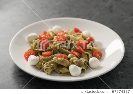 fettuccine with pesto, tomatoes and mozzarella on white plate 67574327