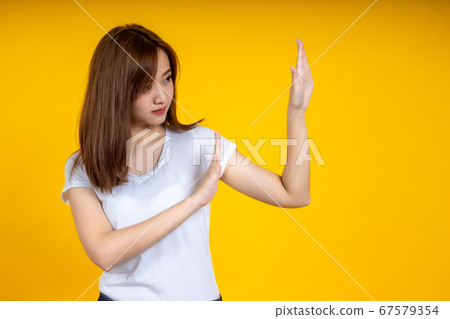 Asian woman making stop gesture isolated on yellow 67579354