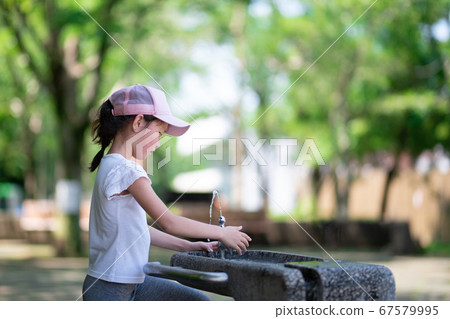 A girl drinking water in a park A girl drinking water in a park 67579995