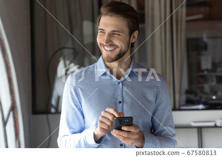 Happy male employee use cellphone looking in distance 67580813