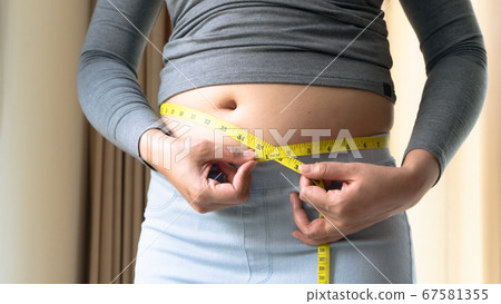 Fat woman hand holding measurement tape on her belly fat. woman diet lifestyle and build muscle Fat woman hand holding measurement tape on her belly fat. woman diet lifestyle and build muscle 67581355