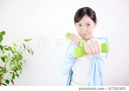 Woman training with dumbbells indoors 67582985