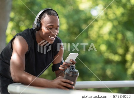 Cheerful black sporty guy chatting on phone, drinking protein Cheerful black sporty guy chatting on phone, drinking protein 67584093