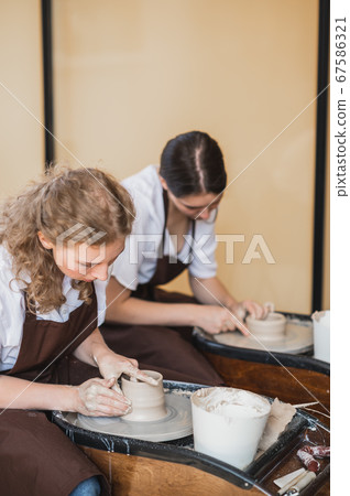 Two girls working on potters wheel making clay handmade craft in pottery workshop, friendship and guidance concept 67586321