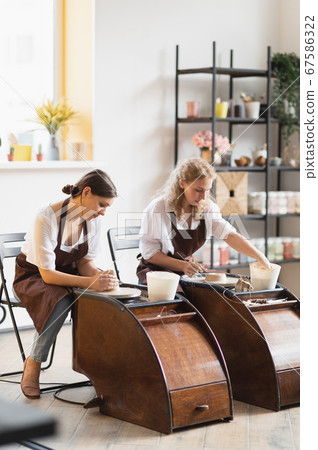 Two female ceramic artists in apron using clay material working in potter studio. Evening freelance distance learning. Adult hobby adventure. Winter educating leisure. Training in modern workshop. 67586322