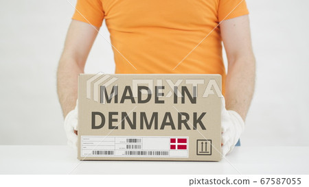 Worker wearing orange uniform puts box with MADE IN DENMARK print on the table 67587055