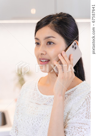 A young woman calling by smartphone at the dining and kitchen A young woman calling by smartphone at the dining and kitchen 67587641