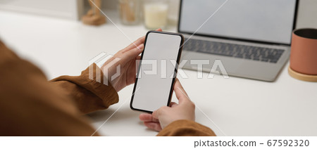 Female holding mock up smartphone while sitting at Female holding mock up smartphone while sitting at 67592320