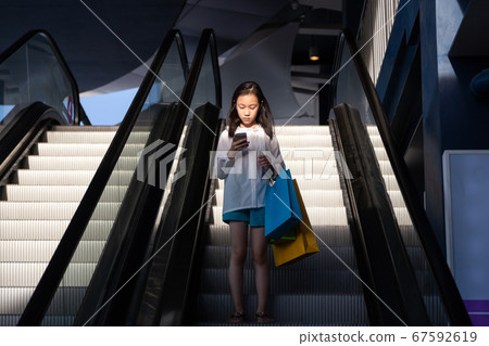 Asian girl on an escalator after a shopping in a store 67592619