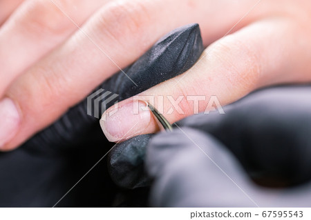 Process manicure close-up. Preparation for hardware manicure. Beautician in rubber gloves cuts the cuticle and processes nails. 67595543
