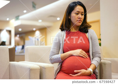 Unhappy pregnant office worker sitting down at the Unhappy pregnant office worker sitting down at the 67598427