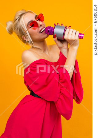 girl in a red elegant dress with bare shoulders with retro glasses holds a microphone and sings 67600814