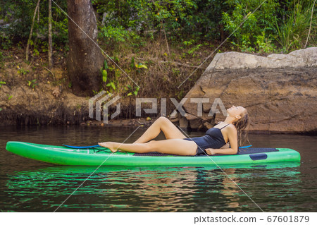 Side view picture of a woman sitting and relaxing on the sup board. Surfer woman resting Side view picture of a woman sitting and relaxing on the sup board. Surfer woman resting 67601879