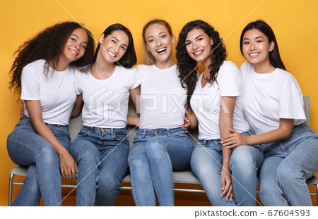 Cheerful Girls Friends Hugging Sitting On Bench On Yellow Background Cheerful Girls Friends Hugging Sitting On Bench On Yellow Background 67604593