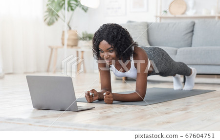 Black girl planking at living room, looking at laptop screen 67604751