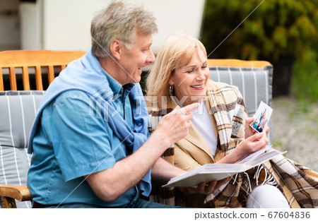 Cheerful senior couple with photo album looking through family pictures on camping trip 67604836