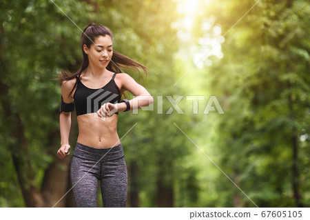 Trail Running Concept. Young man jogging and looking at his smart wrist watch, copy space, outdoor Trail Running Concept. Young man jogging and looking at his smart wrist watch, copy space, outdoor 67605105