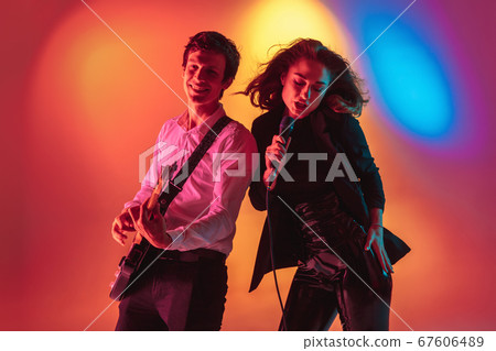 Young caucasian musicians, female singer and guitarist performing on gradient background in neon light. Concept of music, hobby, festival 67606489