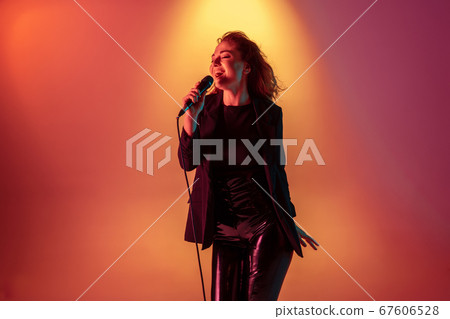 Young caucasian musician, female singer performing on gradient background in neon light. Concept of music, hobby, festival 67606528