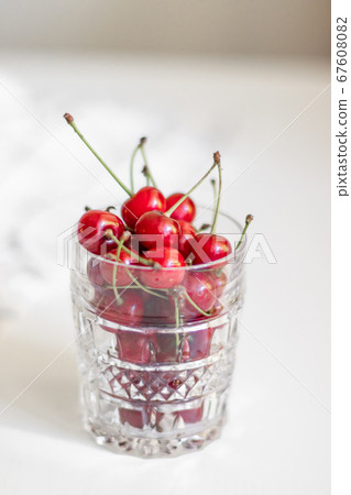 Close-up of glass bowl with ripe cherries stands on a white background with copy space, vertical photo Close-up of glass bowl with ripe cherries stands on a white background with copy space, vertical photo 67608082
