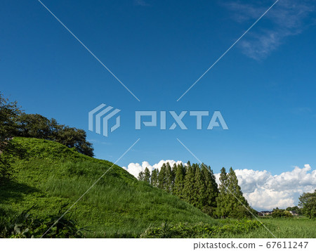 Under the blue sky with clouds in the lush burial mounds in early summer 67611247