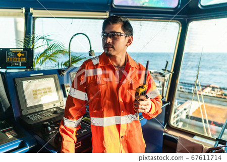 Filipino deck Officer on bridge of vessel or ship. He is speaking on GMDSS VHF radio 67611714