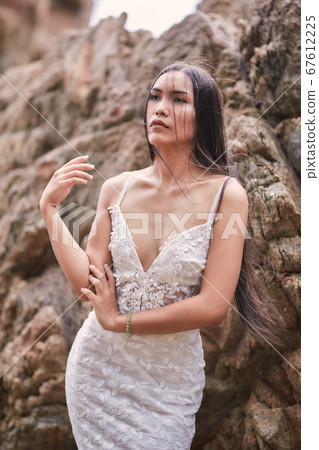 Beautiful asian woman posing on a beach with rocks Beautiful asian woman posing on a beach with rocks 67612225
