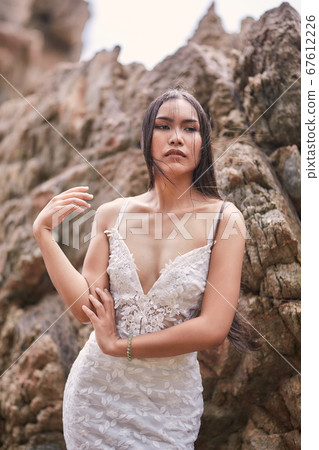 Beautiful asian woman posing on a beach with rocks 67612226
