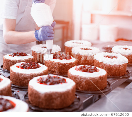 Pastry chef girl makes a cake from fresh biscuit berries and cream. Mass production of cakes and sweets, confectionery factory, professional 67612600