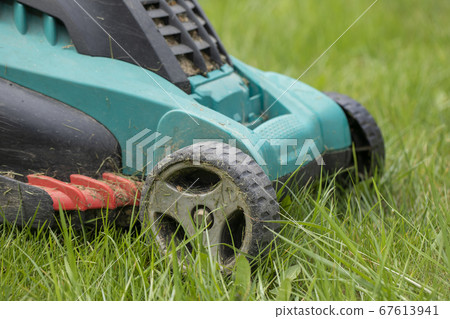 dirty lawn mower stands in stems of green grass dirty lawn mower stands in stems of green grass 67613941
