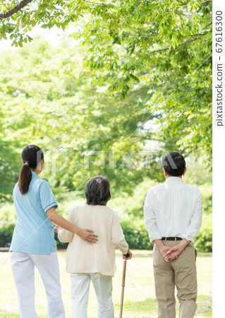 Rear view of senior couple and caregiver rehabilitating outdoors Rear view of senior couple and caregiver rehabilitating outdoors 67616300