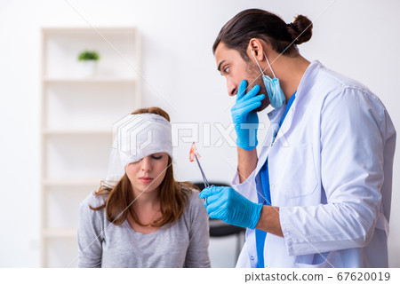 Young head injured woman visiting young male doctor Young head injured woman visiting young male doctor 67620019