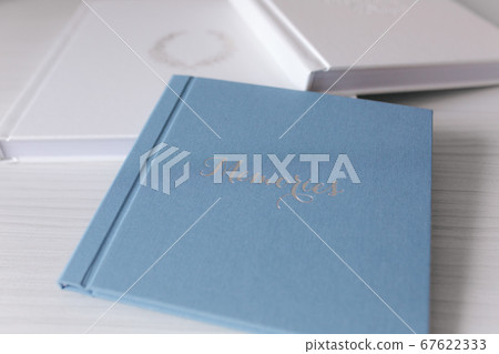 Two closed photobook on white wooden table. Blue and white wedding album with silver embossing Two closed photobook on white wooden table. Blue and white wedding album with silver embossing 67622333