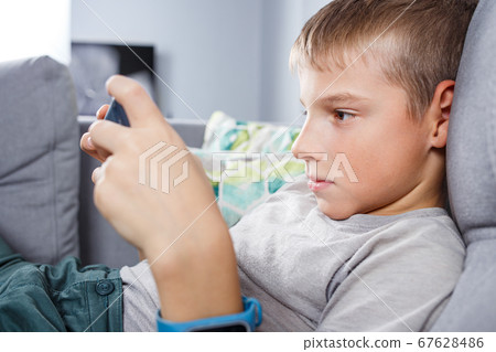 Boy playing games on smartphone sitting at home 67628486
