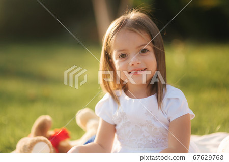 Close up of Adorable little girl sits on plaid outdoors and read book. Happy smiled baby girl spend time on back yard in sunset Close up of Adorable little girl sits on plaid outdoors and read book. Happy smiled baby girl spend time on back yard in sunset 67629768