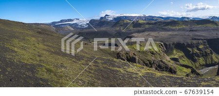Panoramic landscape with blue Markarfljot river canyon, green hills and eyjafjallajokull volcano glacier. Laugavegur hiking trail. Fjallabak Nature Reserve, Iceland. Summer blue sky Panoramic landscape with blue Markarfljot river canyon, green hills and eyjafjallajokull volcano glacier. Laugavegur hiking trail. Fjallabak Nature Reserve, Iceland. Summer blue sky 67639154