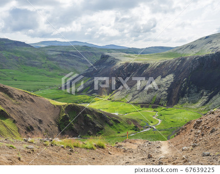 Reykjadalur valley with hot springs river, lush green grass meadow, rocks and hills with geothermal steam. South Iceland near Hveragerdi city. Summer sunny morning, blue sky. Reykjadalur valley with hot springs river, lush green grass meadow, rocks and hills with geothermal steam. South Iceland near Hveragerdi city. Summer sunny morning, blue sky. 67639225
