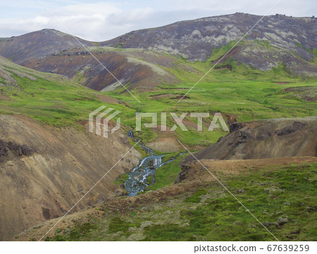 Reykjadalur valley with hot springs river, lush green grass meadow, rocks and hills with geothermal steam. South Iceland near Hveragerdi city. Summer sunny morning, blue sky. Reykjadalur valley with hot springs river, lush green grass meadow, rocks and hills with geothermal steam. South Iceland near Hveragerdi city. Summer sunny morning, blue sky. 67639259