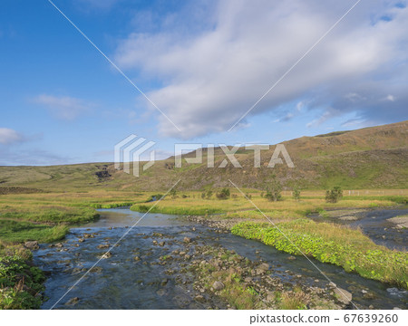 Blue river stream, lush green grass meadow and hills at Reykjadalur hot springs area, South Iceland near Hveragerdi city. Summer sunny morning, blue sky. Blue river stream, lush green grass meadow and hills at Reykjadalur hot springs area, South Iceland near Hveragerdi city. Summer sunny morning, blue sky. 67639260