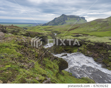 Beautiful lush green Landscape of Skoga river valley cascades near Skogafoss waterfall and Skogar end of Fimmvorduhals hiking trail. South Iceland, Summer blue sky Beautiful lush green Landscape of Skoga river valley cascades near Skogafoss waterfall and Skogar end of Fimmvorduhals hiking trail. South Iceland, Summer blue sky 67639282