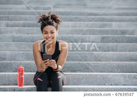 African american girl in sportswear, with wireless headphones and fitness tracker 67639587