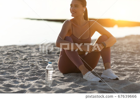 Happy healthy runner sitting on sand, listening to music 67639666