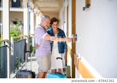 Senior couple with luggage outside apartment on holiday. Senior couple with luggage outside apartment on holiday. 67642162