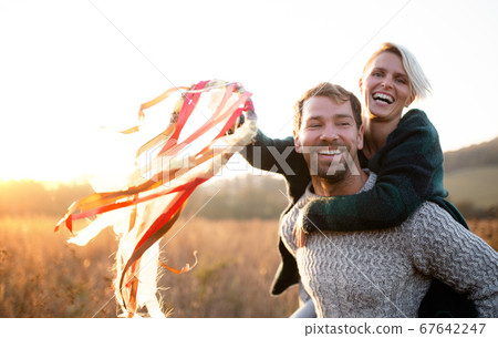 Young couple in love on a walk in autumn forest, holding hand ribbon kites. Young couple in love on a walk in autumn forest, holding hand ribbon kites. 67642247