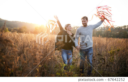 Young couple in love on a walk in autumn forest, holding hand ribbon kites. 67642252