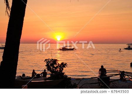 Boracay, Philippines - Jan 27, 2020: Sunset on Boracay island. Sailing and other traditional boats with tourists on the sea against the background of the setting sun. Tourists are sitting on the beach Boracay, Philippines - Jan 27, 2020: Sunset on Boracay island. Sailing and other traditional boats with tourists on the sea against the background of the setting sun. Tourists are sitting on the beach 67643503
