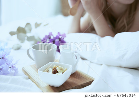 放鬆在一張床上的白色禮服的一名婦女在臥室在一個刷新的早晨 放鬆在一張床上的白色禮服的一名婦女在臥室在一個刷新的早晨 67645014