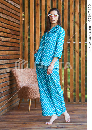 Woman standing in pajamas pajamas with polka dots on wooden background in full length. Caucasian female model. 67647190